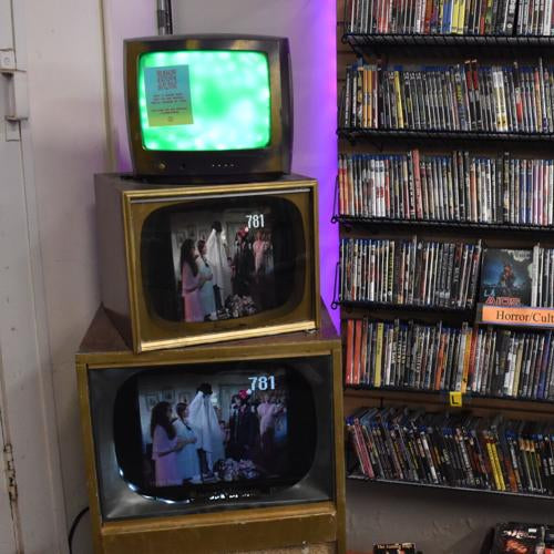 Stack of vintage TVs displaying different images next to a shelf filled with DVDs.